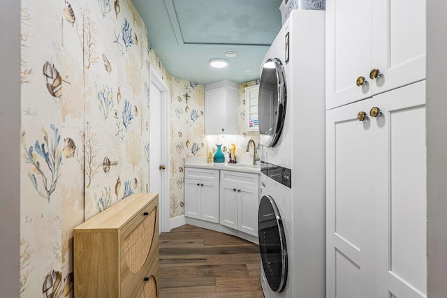 laundry area featuring sink, stacked washer and dryer, cabinets, and dark hardwood / wood-style flooring