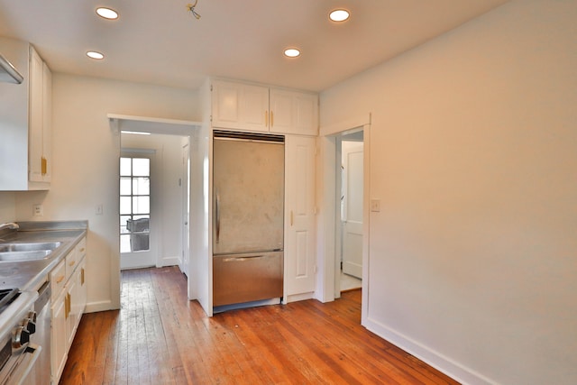 kitchen featuring sink, light wood-type flooring, paneled refrigerator, white cabinets, and range