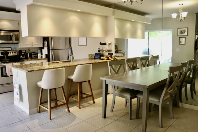 kitchen featuring a breakfast bar area, light stone counters, decorative light fixtures, appliances with stainless steel finishes, and white cabinets