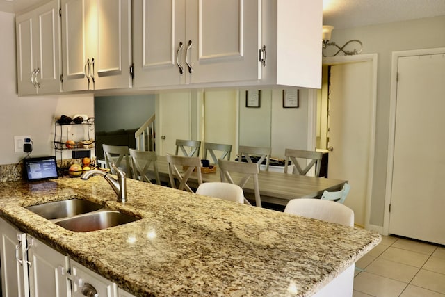 kitchen with light tile patterned flooring, light stone countertops, sink, and white cabinets