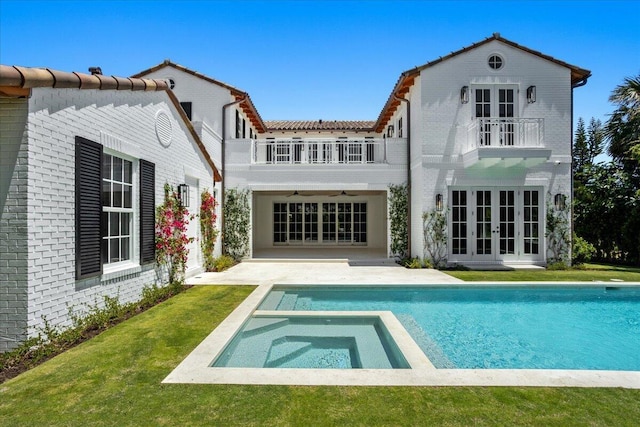 rear view of house featuring a swimming pool with hot tub, a balcony, a patio, and french doors