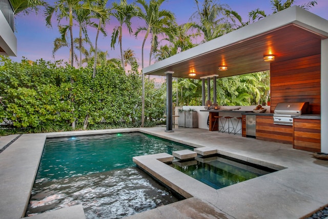 pool at dusk with a grill, area for grilling, and a patio area