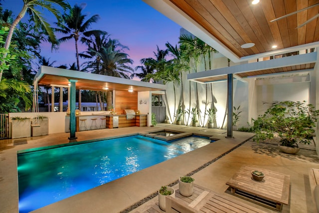 pool at dusk with an in ground hot tub, area for grilling, and a patio area