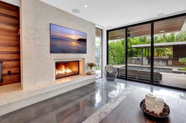 living room with a wall of windows, ceiling fan, and concrete flooring