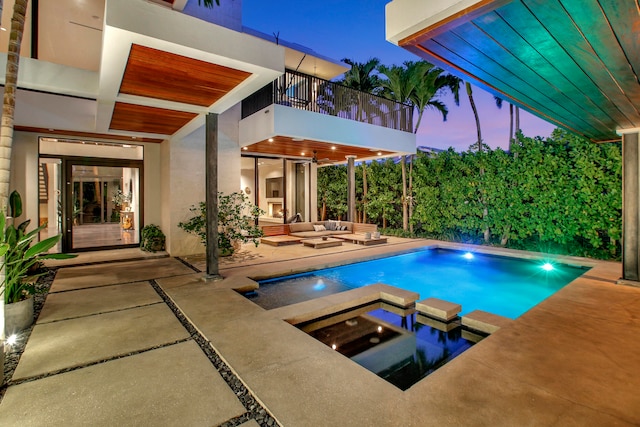 pool at dusk featuring a patio area and an in ground hot tub