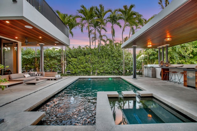 pool at dusk with an outdoor hangout area, an outdoor bar, an outdoor kitchen, an in ground hot tub, and a patio