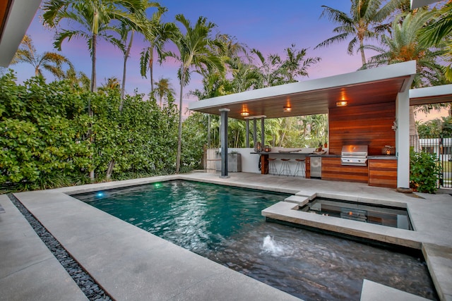 pool at dusk with a patio area, an outdoor kitchen, and a grill