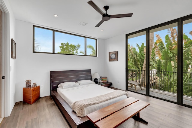 bedroom featuring access to exterior, ceiling fan, a wall of windows, and light hardwood / wood-style flooring