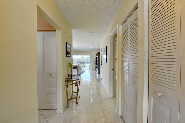 hallway with a textured ceiling and light tile patterned floors