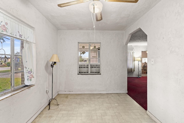 empty room with a textured ceiling, light tile flooring, and ceiling fan