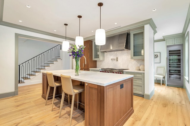 kitchen featuring light hardwood / wood-style flooring, tasteful backsplash, custom range hood, hanging light fixtures, and a kitchen island with sink