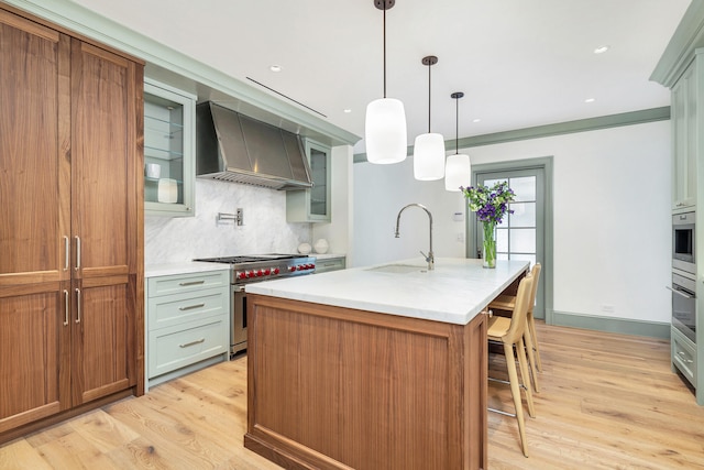 kitchen with wall chimney range hood, light hardwood / wood-style flooring, luxury range, a center island with sink, and tasteful backsplash