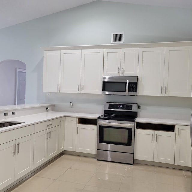 kitchen featuring lofted ceiling, appliances with stainless steel finishes, sink, light tile floors, and white cabinets