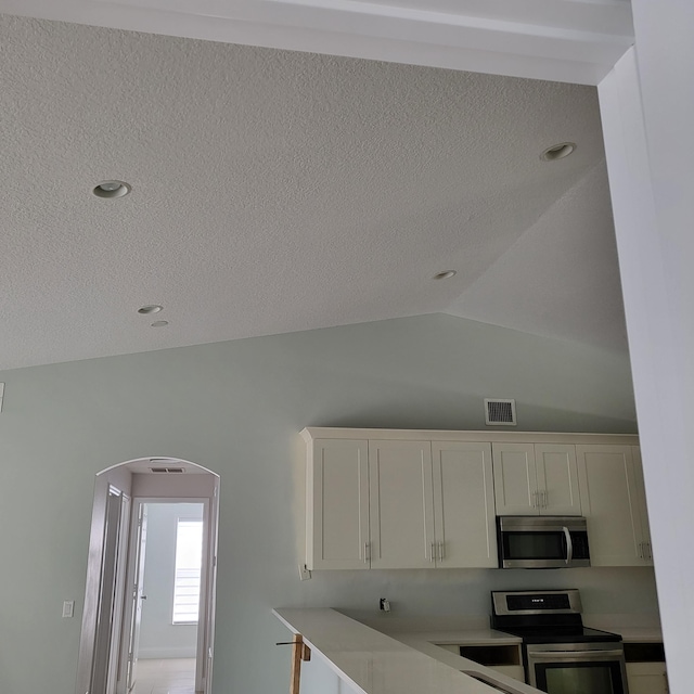 kitchen with white cabinets, a textured ceiling, vaulted ceiling, and appliances with stainless steel finishes