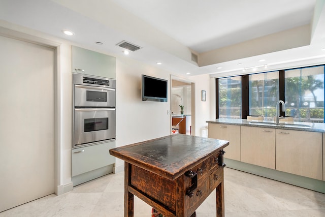 kitchen with cream cabinetry, light stone counters, double oven, and sink