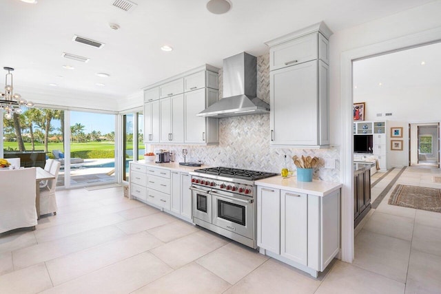 kitchen with double oven range, wall chimney exhaust hood, a chandelier, and a healthy amount of sunlight