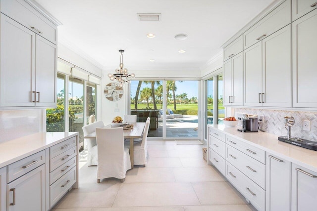 kitchen with light tile floors, tasteful backsplash, crown molding, hanging light fixtures, and an inviting chandelier