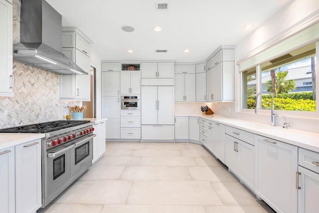 kitchen with light tile floors, white cabinets, backsplash, premium appliances, and wall chimney range hood