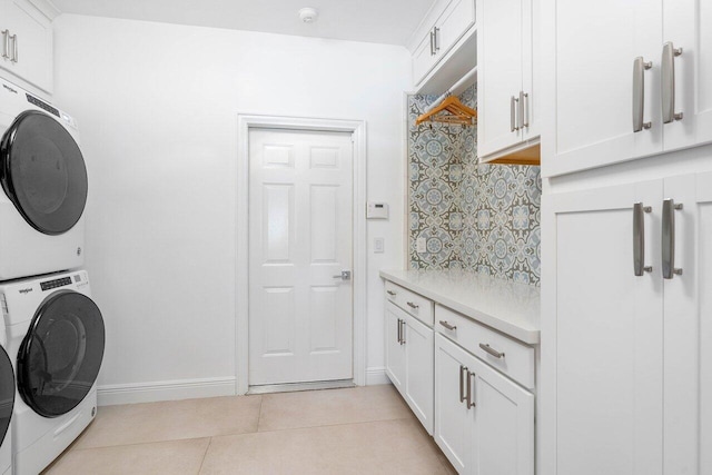 clothes washing area featuring light tile floors, cabinets, and stacked washer and dryer