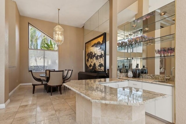 bar with light stone countertops, sink, hanging light fixtures, white cabinets, and an inviting chandelier