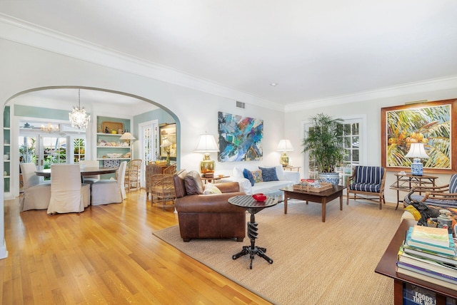 living room with an inviting chandelier, crown molding, built in features, and light hardwood / wood-style flooring