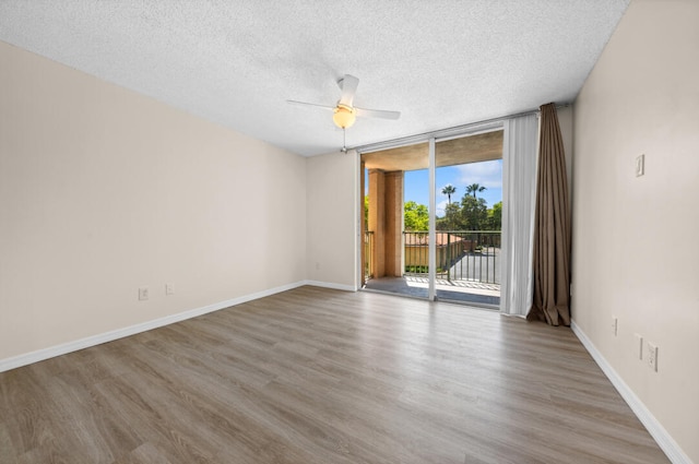 spare room featuring a textured ceiling, a wall of windows, ceiling fan, and light wood-type flooring