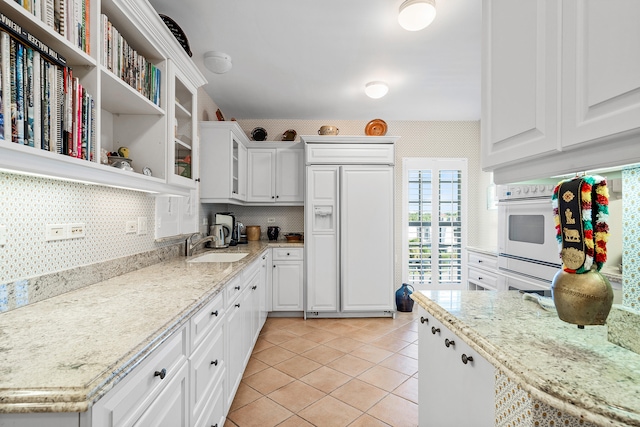 kitchen featuring backsplash, paneled built in fridge, white cabinets, sink, and light tile floors