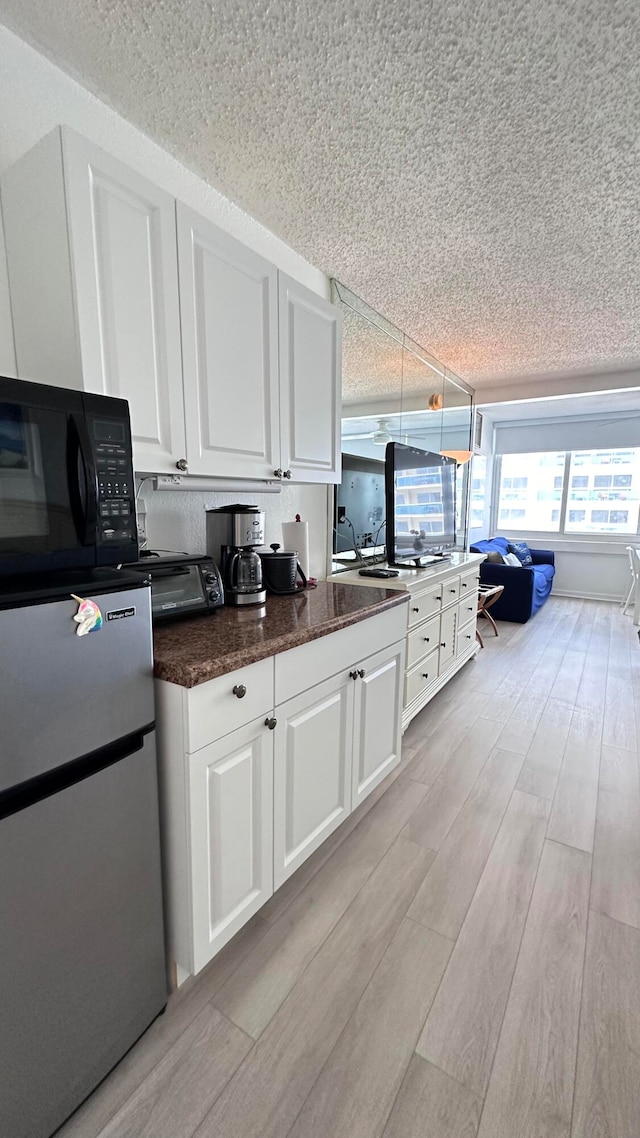 kitchen featuring pendant lighting, light hardwood / wood-style floors, a textured ceiling, white cabinetry, and stainless steel refrigerator