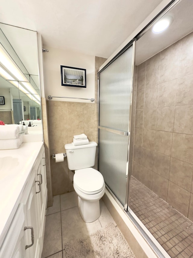 bathroom featuring tile walls, toilet, a shower with shower door, tile flooring, and vanity