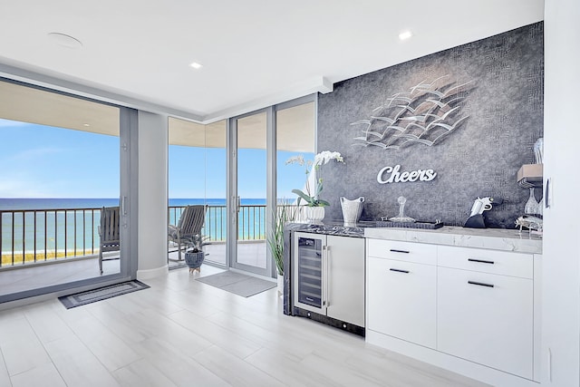 kitchen with white cabinetry, a water view, light stone counters, backsplash, and floor to ceiling windows