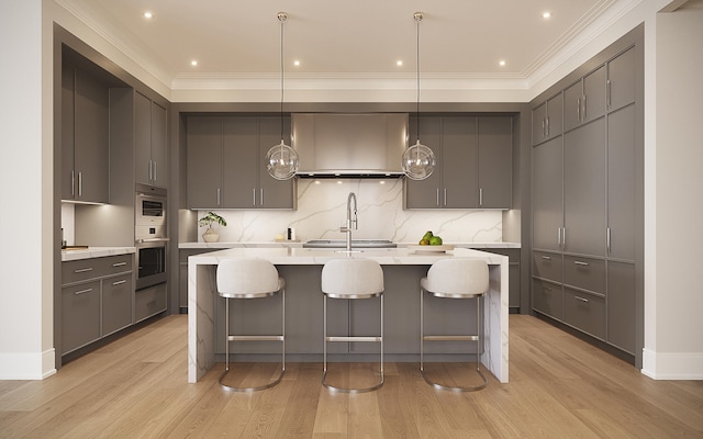 kitchen featuring light wood-type flooring, pendant lighting, gray cabinets, backsplash, and a center island with sink