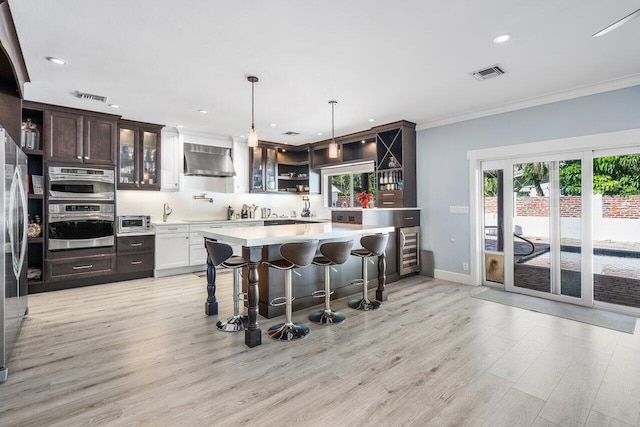 kitchen with wall chimney range hood, a kitchen breakfast bar, light hardwood / wood-style floors, and hanging light fixtures