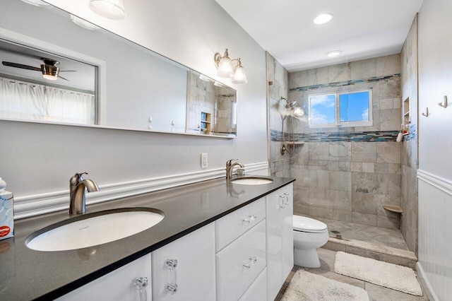 bathroom with ceiling fan, dual sinks, tiled shower, toilet, and oversized vanity