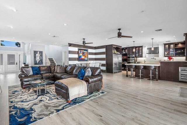 living room with light hardwood / wood-style floors, ceiling fan, and beverage cooler