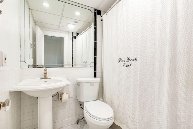 bathroom with a paneled ceiling, tile flooring, toilet, and tile walls