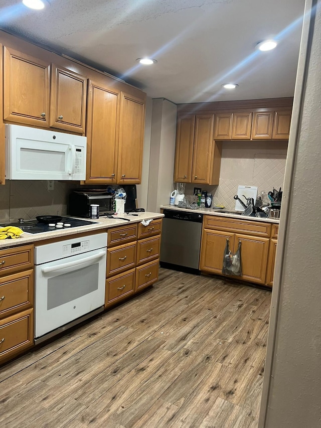 kitchen with white appliances, tasteful backsplash, sink, and light wood-type flooring