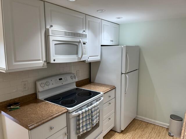 kitchen with light hardwood / wood-style flooring, tasteful backsplash, white appliances, and white cabinetry