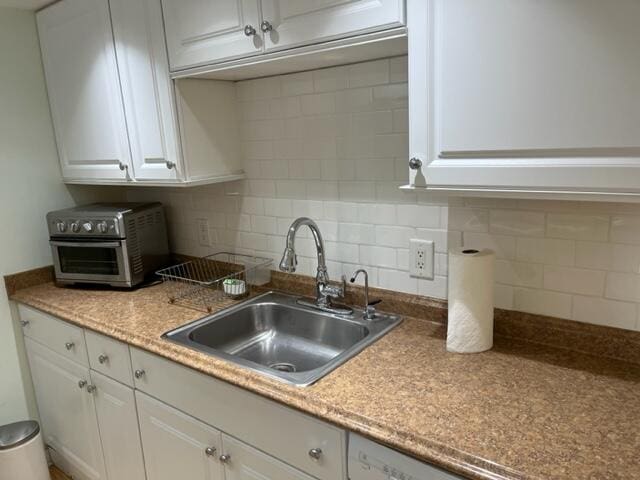 kitchen with light stone countertops, white cabinetry, backsplash, and sink