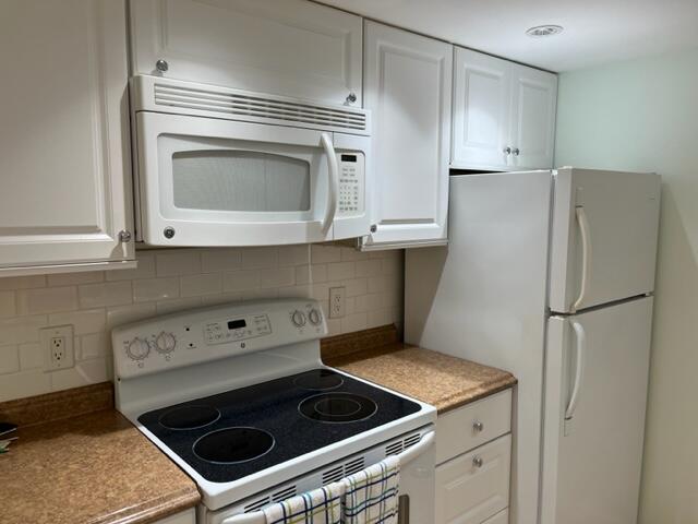 kitchen with backsplash, white appliances, and white cabinets