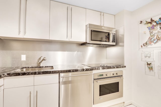 kitchen with white cabinetry, backsplash, sink, stainless steel appliances, and dark stone counters