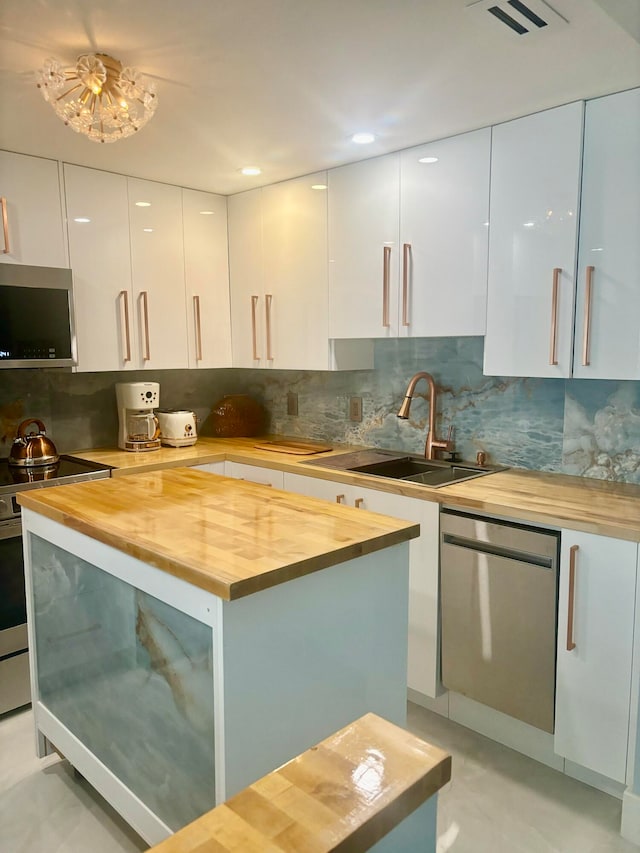 kitchen with sink, stainless steel appliances, wood counters, tasteful backsplash, and white cabinets