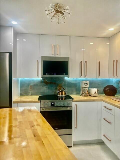 kitchen with decorative backsplash, butcher block counters, white cabinetry, and stainless steel appliances