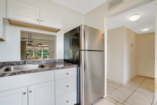 kitchen featuring stainless steel fridge, light tile floors, white cabinetry, and sink