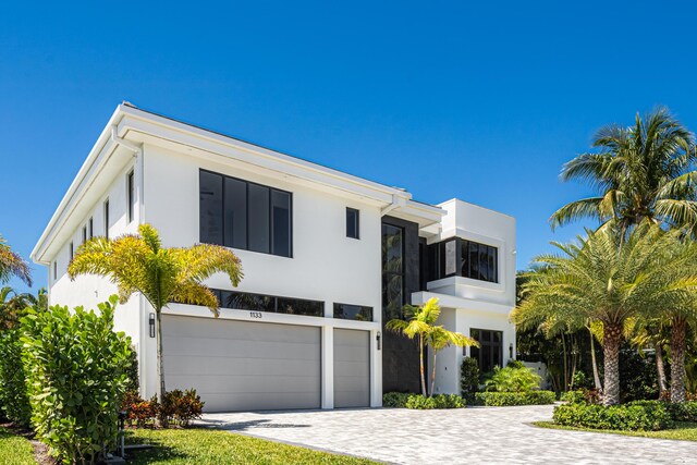 modern home featuring decorative driveway, fence, a garage, and stucco siding