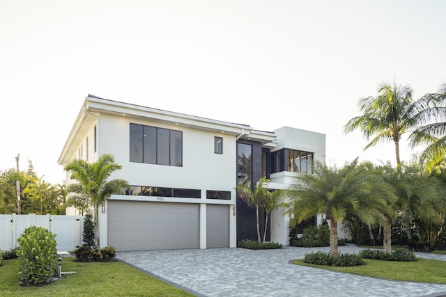 contemporary house featuring fence, stucco siding, a front lawn, a garage, and decorative driveway