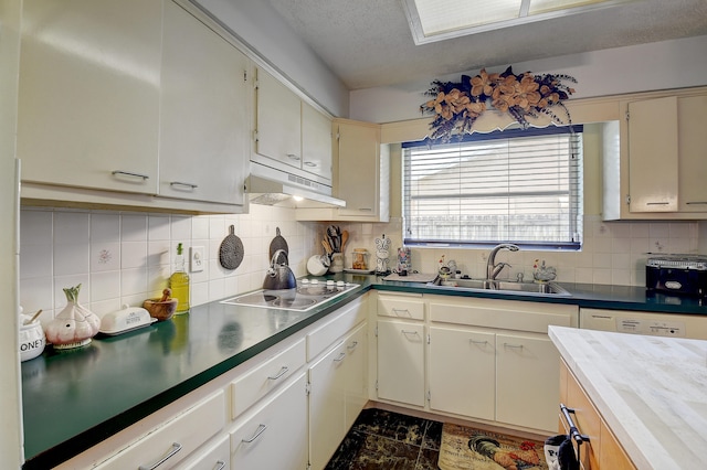 kitchen featuring a textured ceiling, tasteful backsplash, black electric stovetop, dark tile floors, and sink