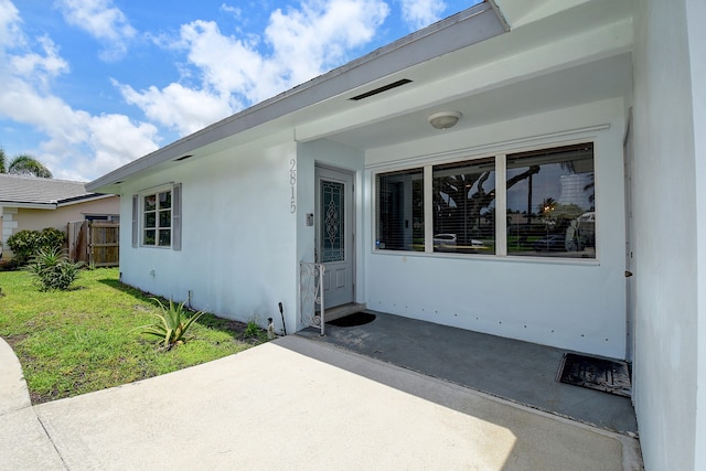 view of exterior entry with a lawn and a patio area