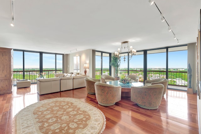 living room featuring hardwood / wood-style floors, a wall of windows, track lighting, and an inviting chandelier