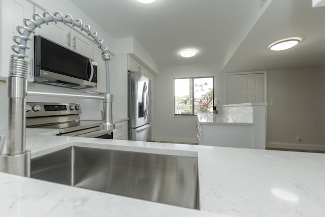 kitchen with stainless steel appliances, white cabinetry, and light stone counters