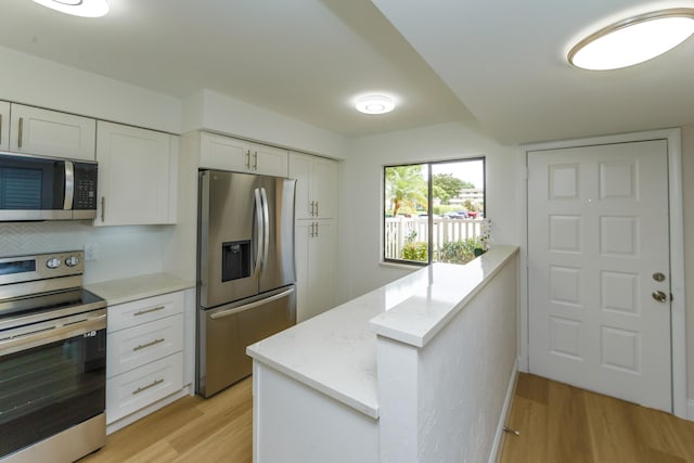 kitchen with white cabinets, light hardwood / wood-style flooring, appliances with stainless steel finishes, and light stone counters